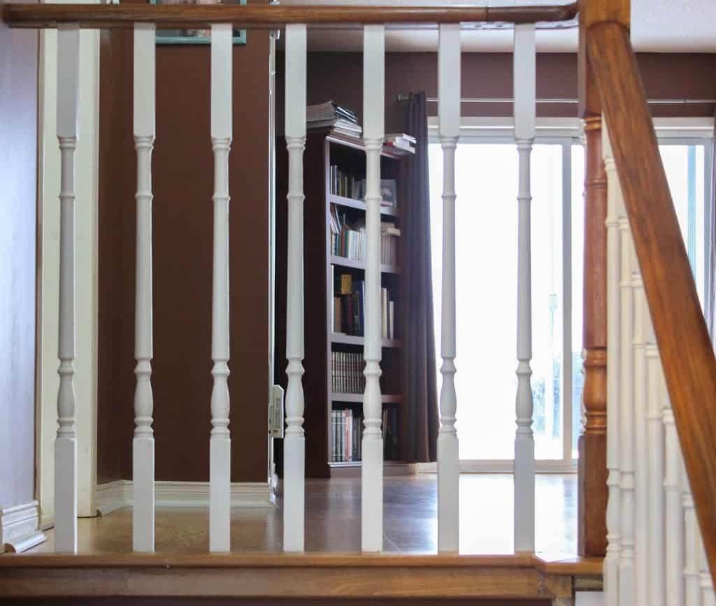 Brown and white railing, bookshelf and window in the background