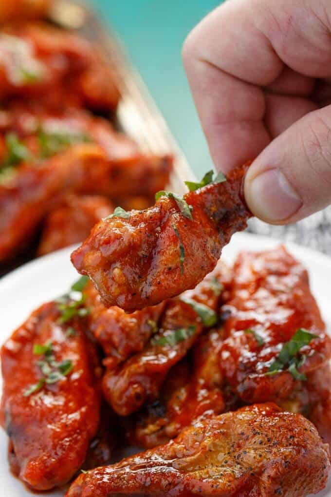 Baked Sriracha Chicken Wings on white plate and tray, one wing held by hand
