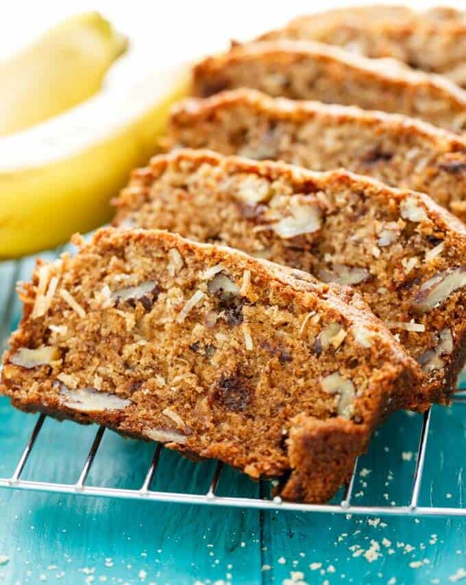 Chocolate Chip Banana Bread with Coconut and Nuts sliced near banana and on blue background