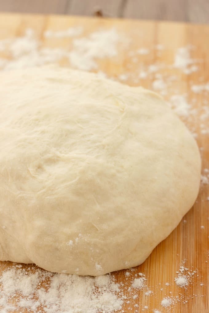 Homemade Pizza Dough on wooden pad with spilled flour around