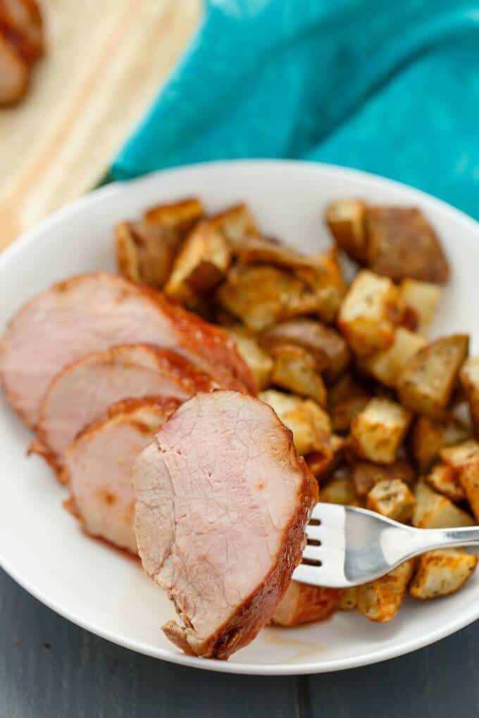 Honey glazed pork tenderloin pork dish on white plate, pork slice picked on fork