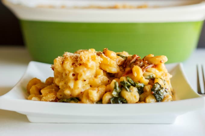 Macaroni and Cheese with Sun-dried Tomatoes and Spinach on white plate on table, bowl in background