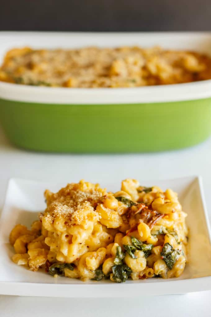 Macaroni and Cheese with Sun-dried Tomatoes and Spinach on white plate on table, bowl in background