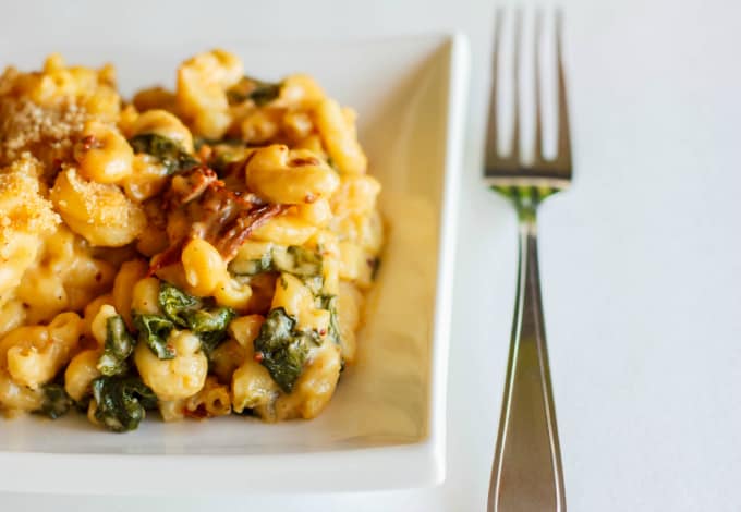 Macaroni and Cheese with Sun-dried Tomatoes and Spinach on whjite plate, next to fork on white background