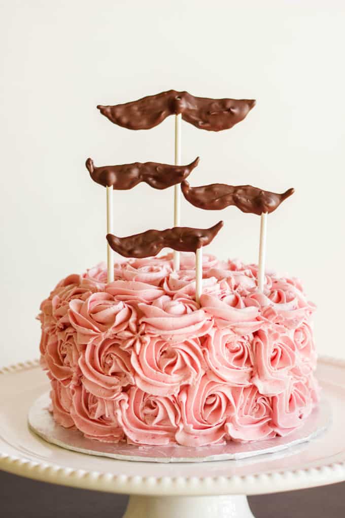 Raspberry Swiss Meringue Buttercream cake on white stray with chocolate accesories in sticks