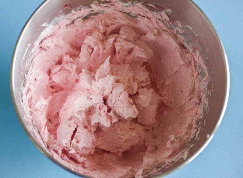 Pink buttercream in bowl, blue background