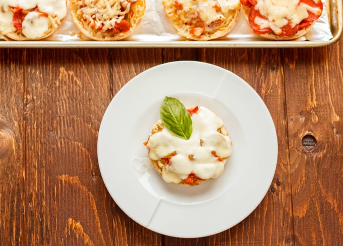 Mini Pizzas on English Muffins on white plate on wooden table, muffins on tray in the background