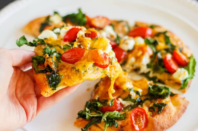 Naan Bread Pizza on white plate, pizza slice held by hand