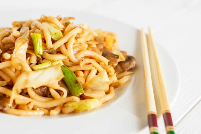 Fried Udon Noodles with Mushrooms and Cabbage on white plate and sticks