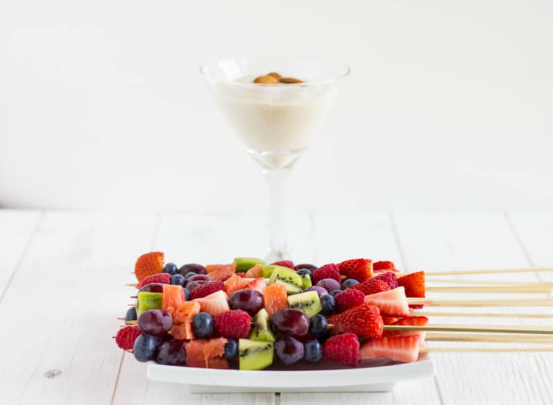 Fruit kabobs on white plate with almond whipped cream with almonds in glass on white table