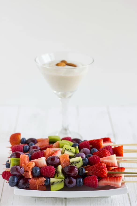 Fruit kabobs on white plate with almond milk cream in glass on white table