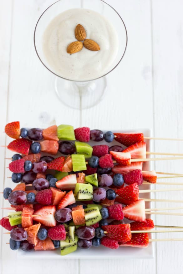 Fruit kabobs on white plate with almond whipped cream with almonds in glass on white table