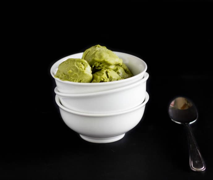 Vegan green tea ice cream in white bowl next to spoon on black background