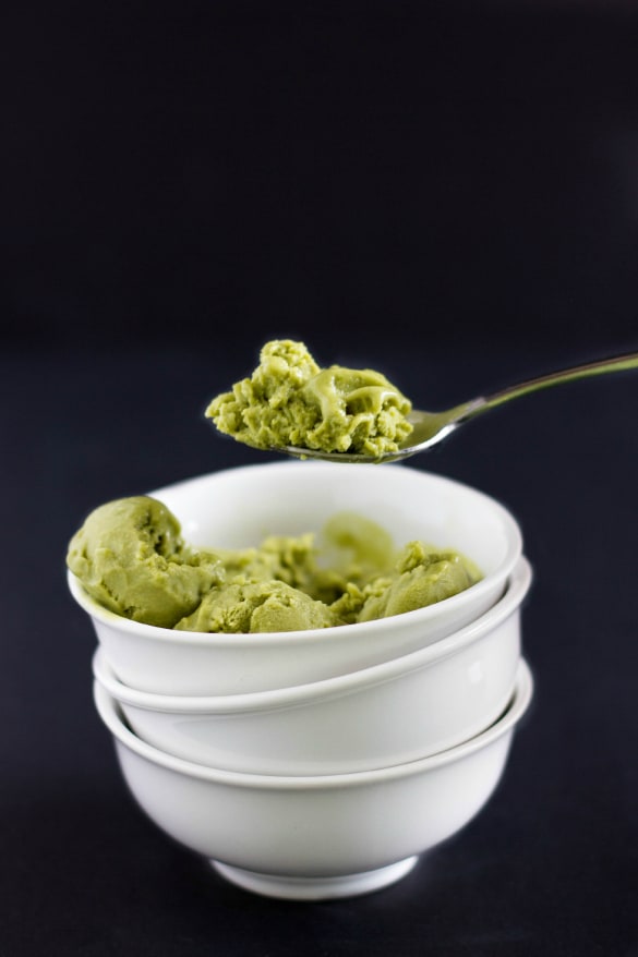 Vegan green tea ice cream in white bowl picked up by sppon on black background
