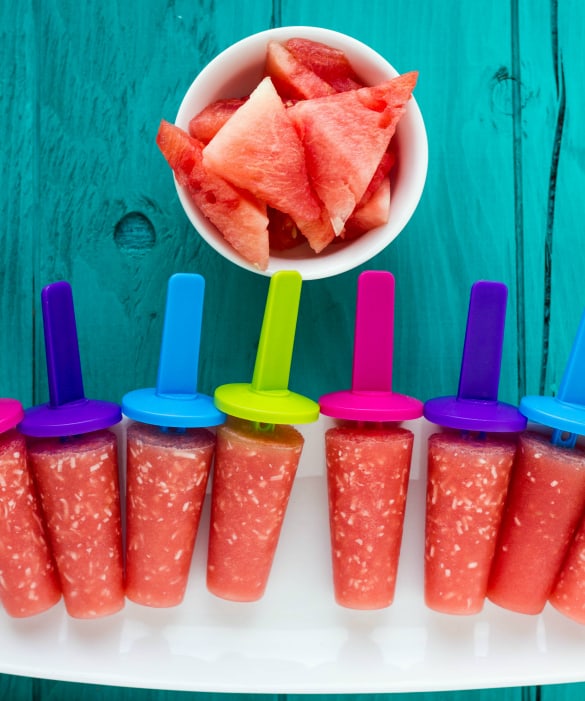 Watermelon and coconnut popsicles with sliced watermelon in bowl on blue table
