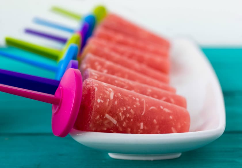 Watermelon and coconut popsicles on white plate on blue table