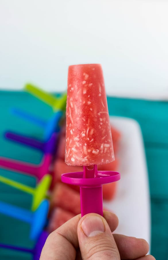 Hand holding watermelon and coconut posile, popsicles in the background