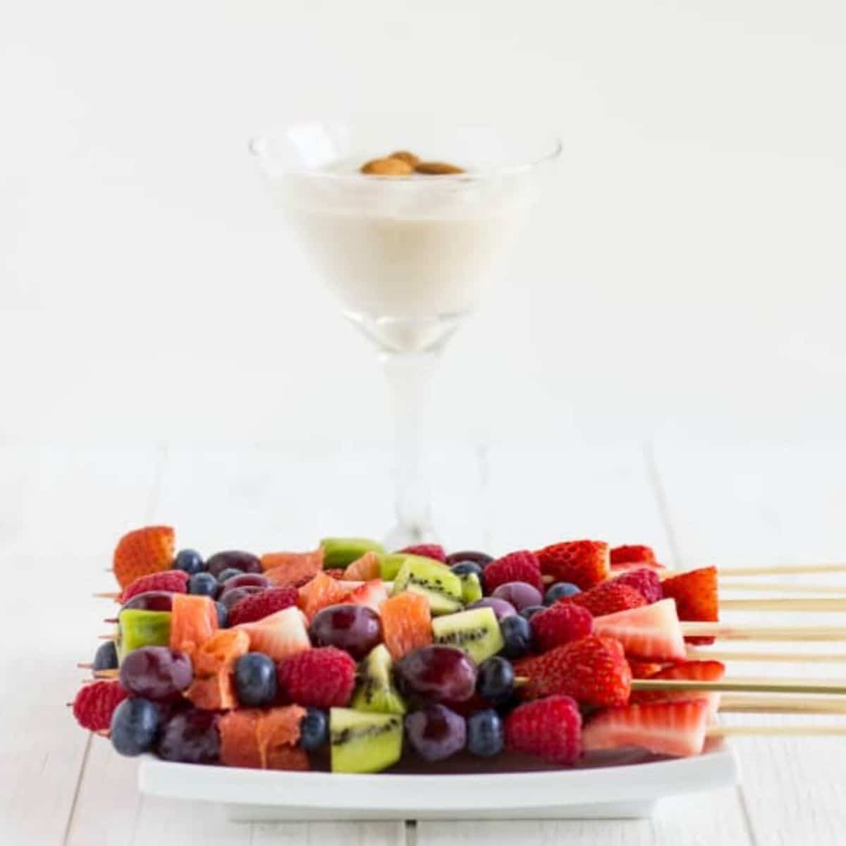 Fruit kabobs on white plate with almind milk cream in glass