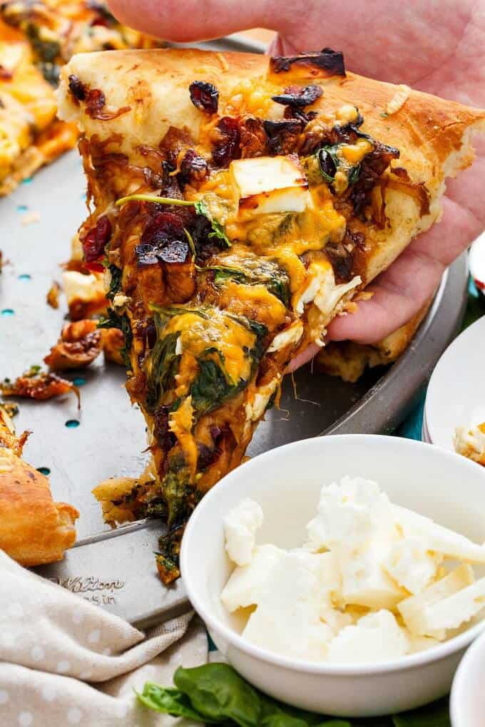 Caramelized Onion Dried Fig Pizza with Feta sliced and held by hand with bowl  full of accessories