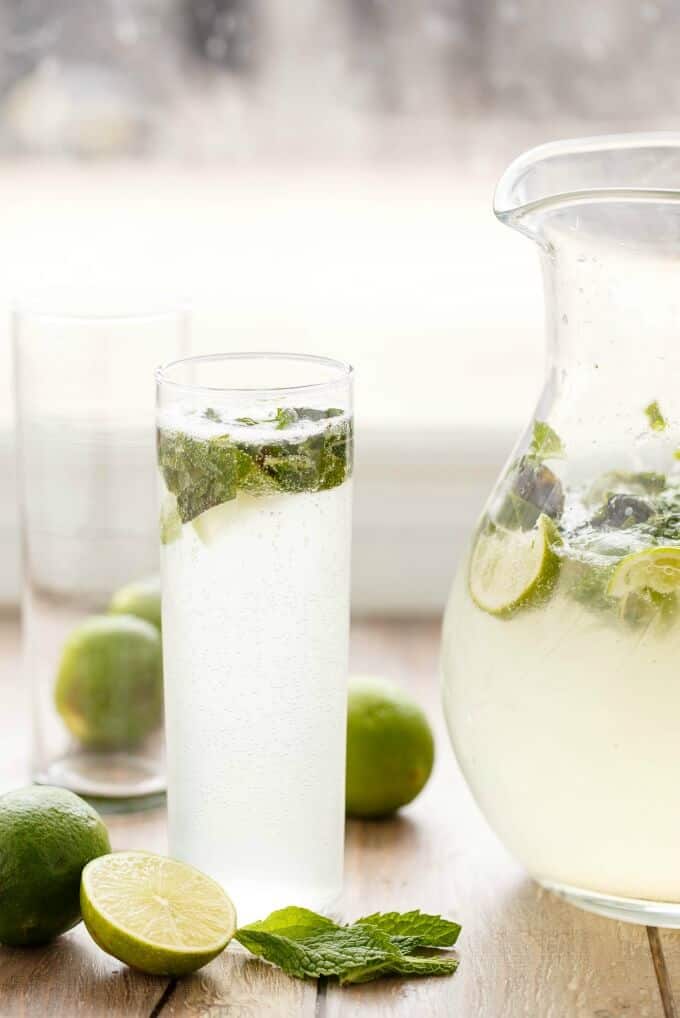 Half Pitcher of Mojitos in glass shot and glass pitcher on table with limes