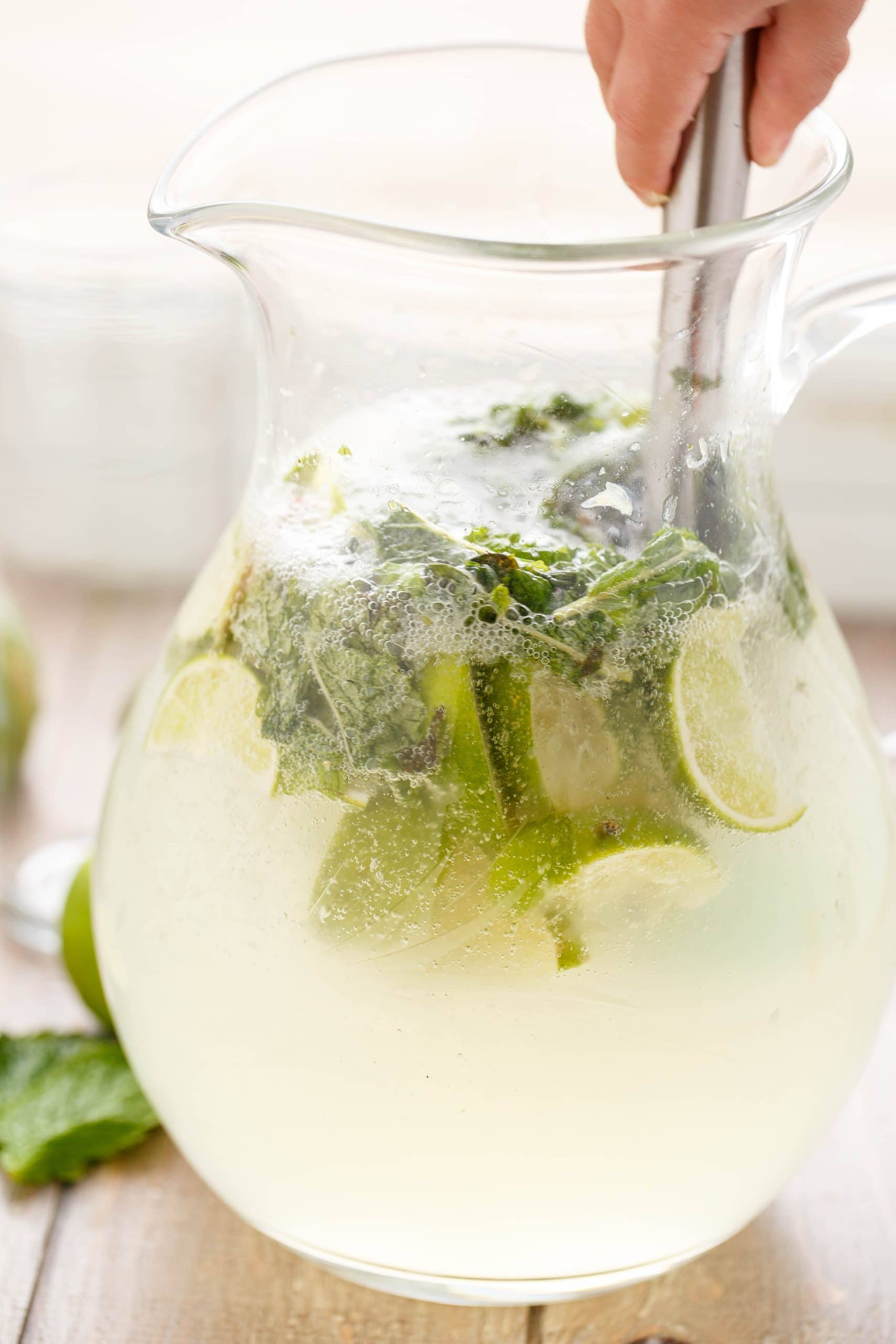 Mojito being hand mixed in pitcher with sliced lemons