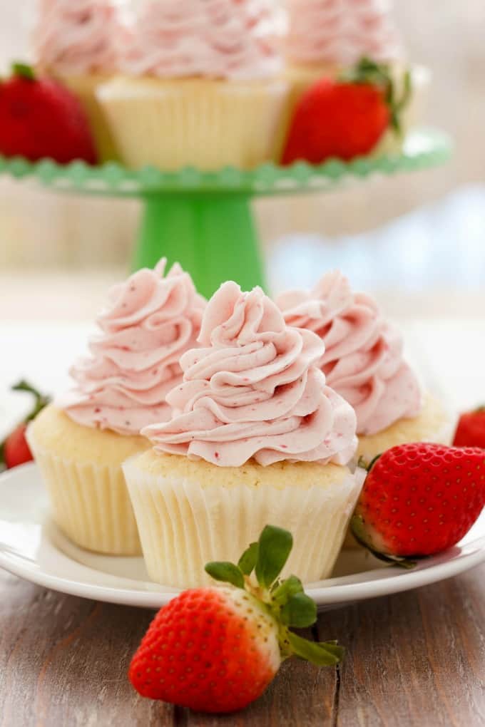 Lemon Cupcakes with Strawberry Swiss Meringue Buttercream on white plate next to strawberries , stray with cupcakes  in the background#cupcakes