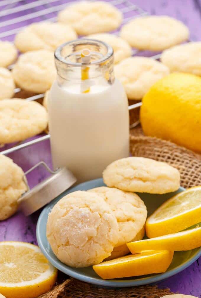 Lemon and Almond Cookie Crinkles on baking grid, blue plate with  slices of lemon,  glass jar of milk and whole lemon