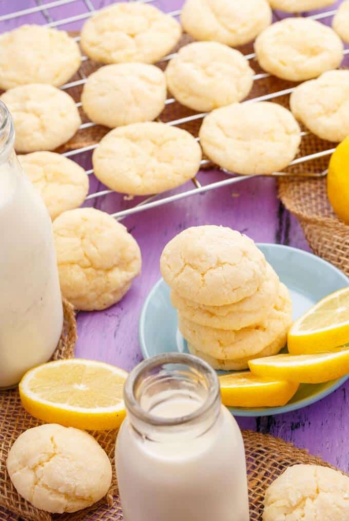 Lemon and Almond Cookie Crinkles on table and blue small plate nexto to lemons and bottle of milk