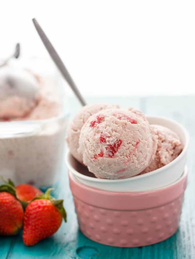 Strawberry Banana Ice Cream  in white bowl on blue table with ripe strawberries and rest of ice cream in the background#strawberry