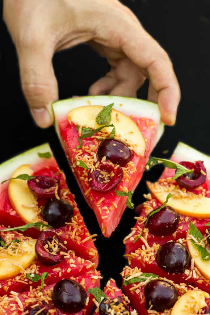 Healthy vegan watermelon pizza dessert slices , one slice held by hand