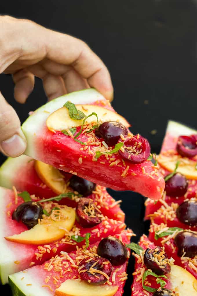 Healthy Vegan Watermelon Pizza Dessert sliced and hel by hand, black background