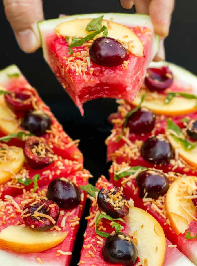 Healthy Vegan Watermelon Pizza Dessert sliced and held by hand, black background