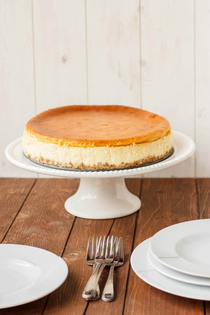 New York Style Cheesecake with Strawberry Topping on white stray next to forks and white plates on wooden table