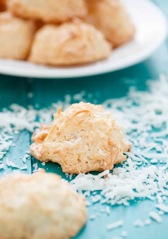 Semi-Toasted Coconut Macaroons on bluetable sprinkled by sliced coconut around#cookies