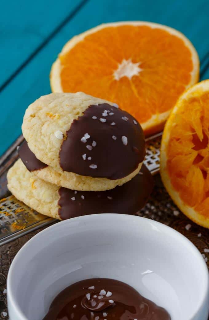 Chocolate Dipped Orange Cookie Crinkles with sliced oranges and chocolate dip in white bowl on blue table