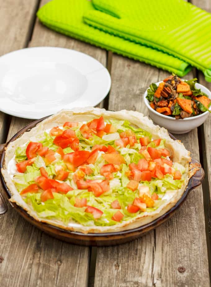 Gluten-Free and Vegan Taco Pie on glass big plate on wooden table next to white plate and bowl full of tacos and kitchen gloves