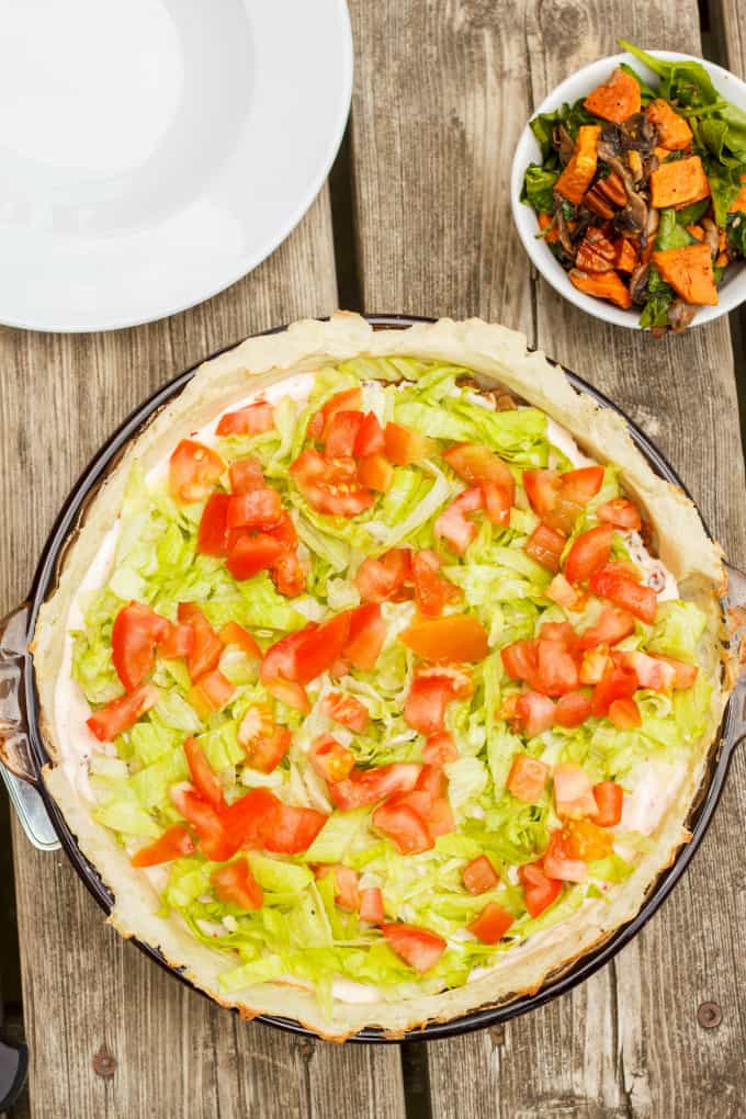 Gluten-Free and Vegan Taco Pie on plate on wooden table next to white plate and bowl full of tacos