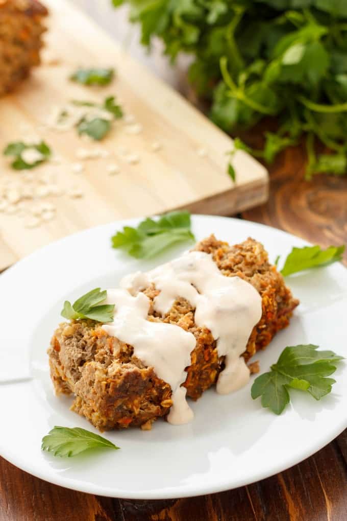 Mexican Meat Loaf with Sour Cream on white plate with veggies next to wooden kitchen pad on  brown table