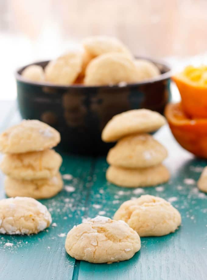 Orange cookie crinkles on blue table, black bowl full of cookies in the background