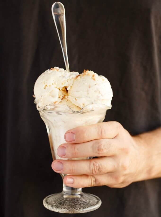 Toasted Coconut Ice Cream in glass held by hand with glass spoon on black background#dessert