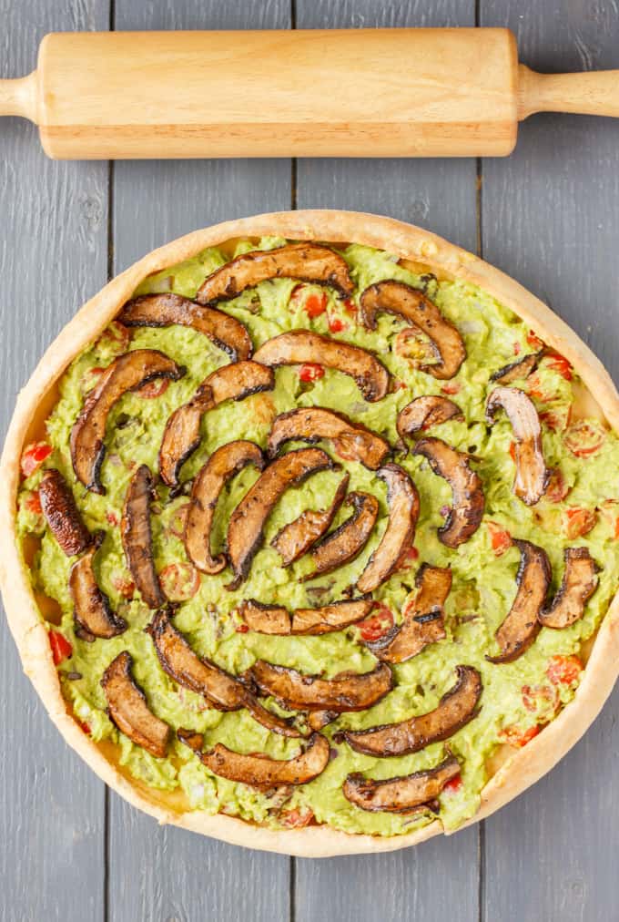 Vegan Guacamole Pizza on wooden table  next to wooden kitchen roller