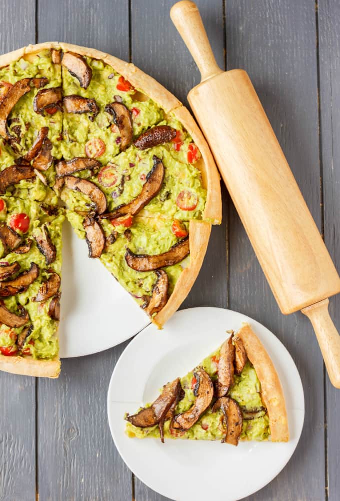 Vegan Guacamole Pizza on white plates on wooden table and kitchen wooden roller