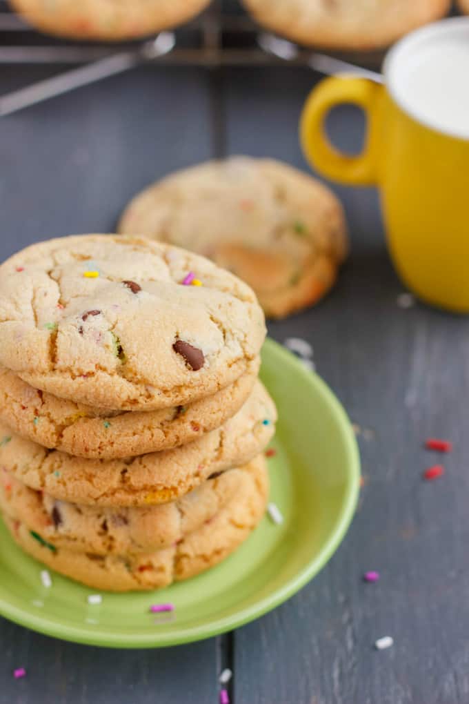 Birthday Cake Chocolate Chip Cookies on small green yellow on black table, cookies and yellow mug in the background