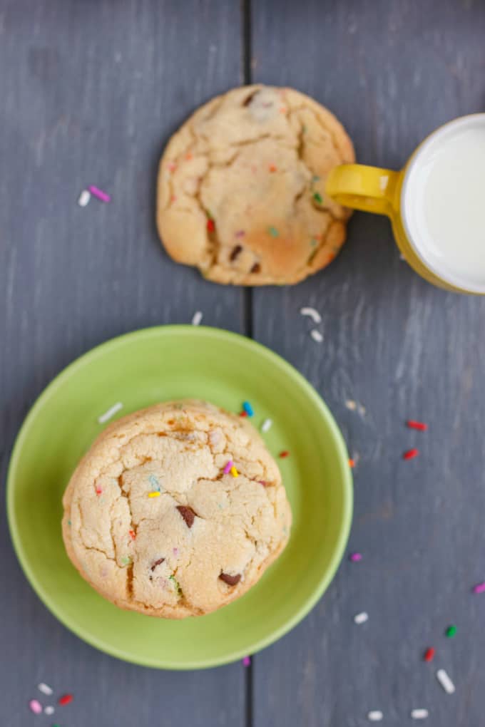 Birthday Cake Chocolate Chip Cookies on green plate on black table with cookie and yelow mug with milk