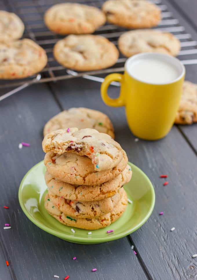 Birthday Cake Chocolate Chip Cookies on small green plate on black table with yellow mug with milk and cookies in the background