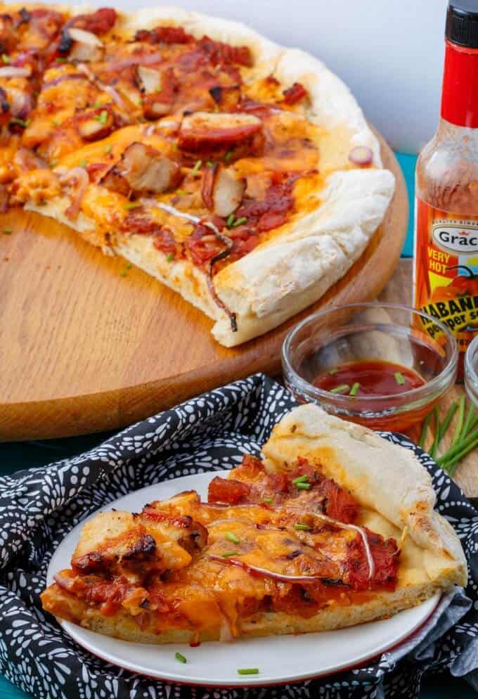 BBQ Chicken Pizza with Mushrooms and Onions on pizza pad, slice on white plate nexto to spicy sace in bowl and bottle