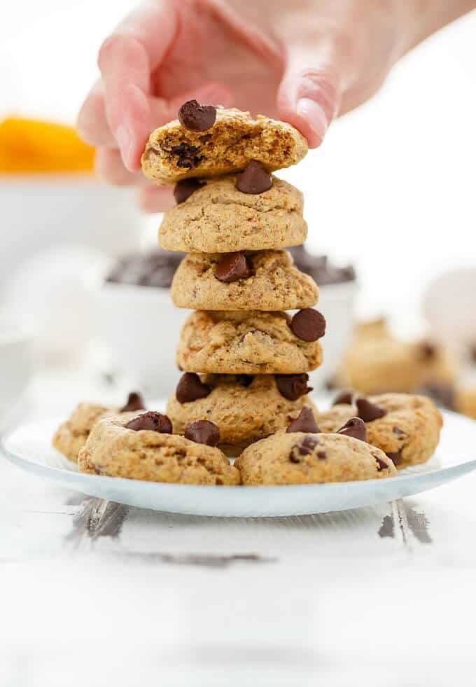 Chocolate Chip Pumpkin Cookies stacked and held by hand on white plate on table