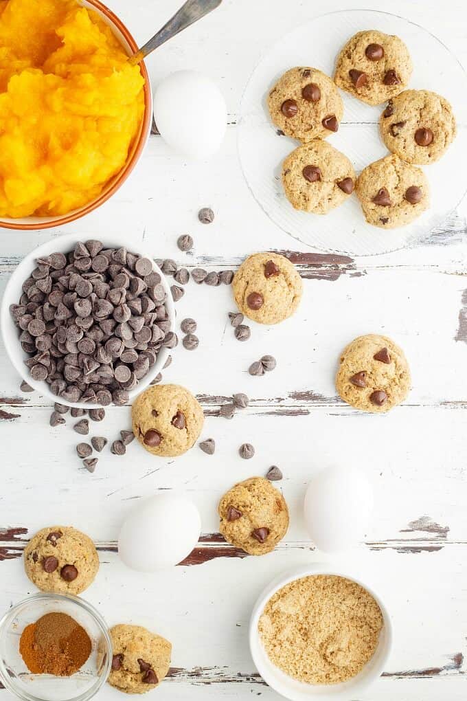 Chocolate Chip Pumpkin Cookies on table next to bowl of chocolate chips, mashed pumpkin nad ingredients in small bowls on table