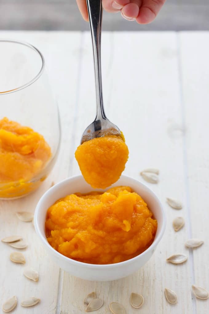 Homemade Pumpkin Puree in white bowl, glass jar and spoon on white table with pumkpkin seeds#vegan