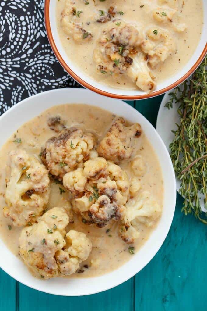 Roasted Cauliflower Soup in white bowls on blue table next to herbs